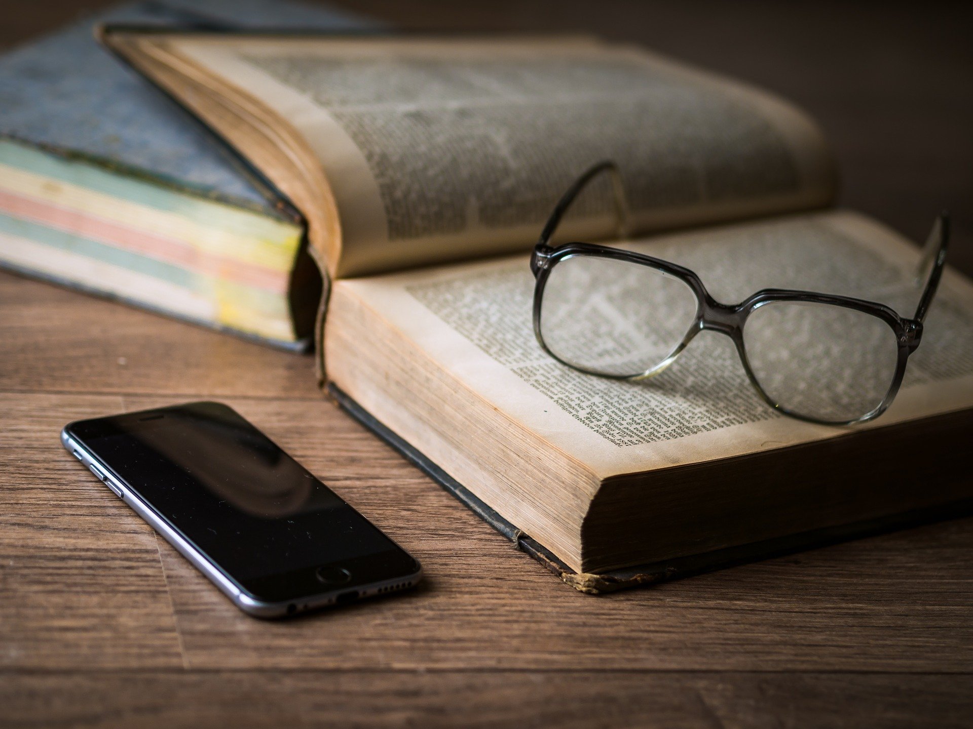 Foto von Smartphone, welches neben Buch und Brille liegt